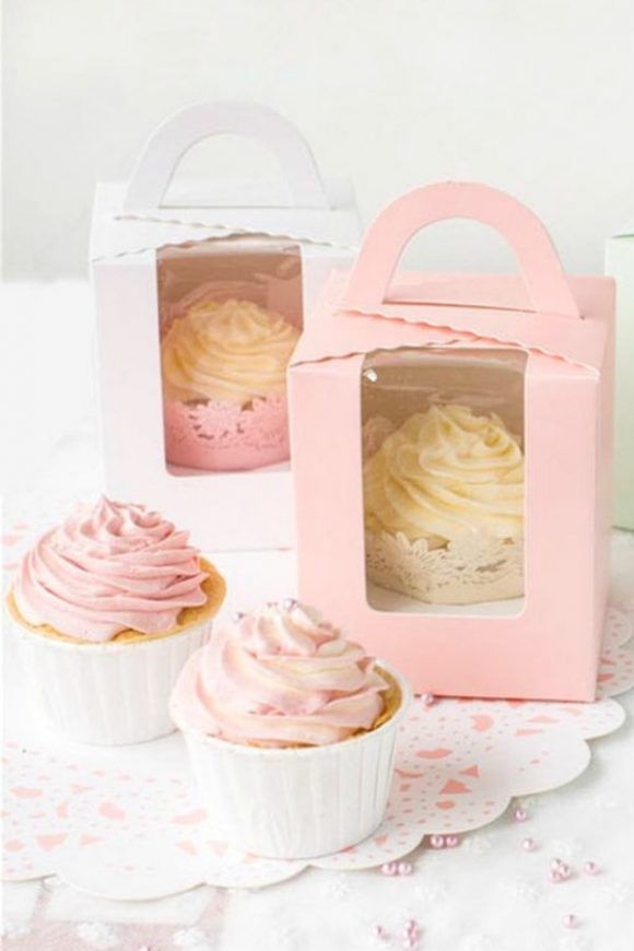 there are four cupcakes in small boxes on the table with pink frosting