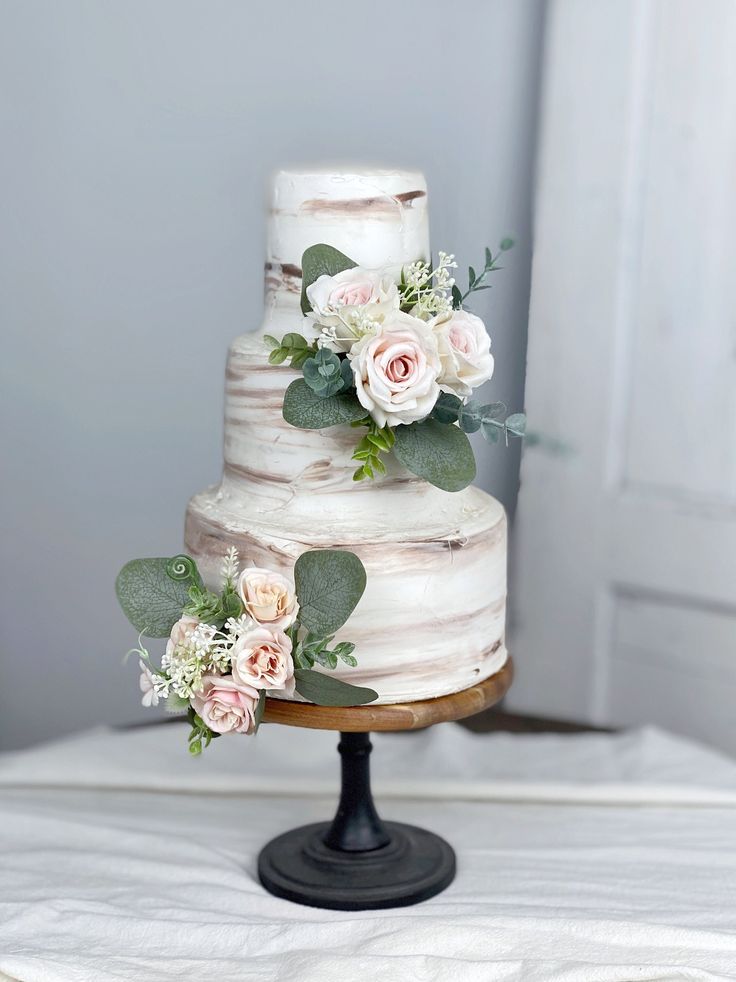 a three tiered wedding cake with flowers on top and greenery around the edges