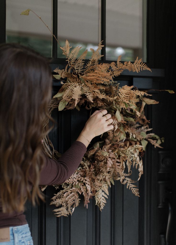 a woman is holding a wreath on the front door to show it's fall foliage