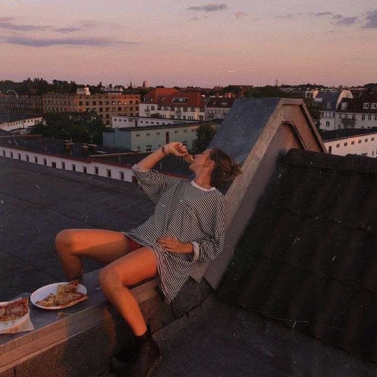 a woman sitting on top of a roof next to a plate of food and drink