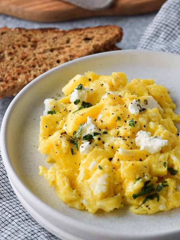 scrambled eggs with cheese and herbs on a white plate next to slices of toasted bread