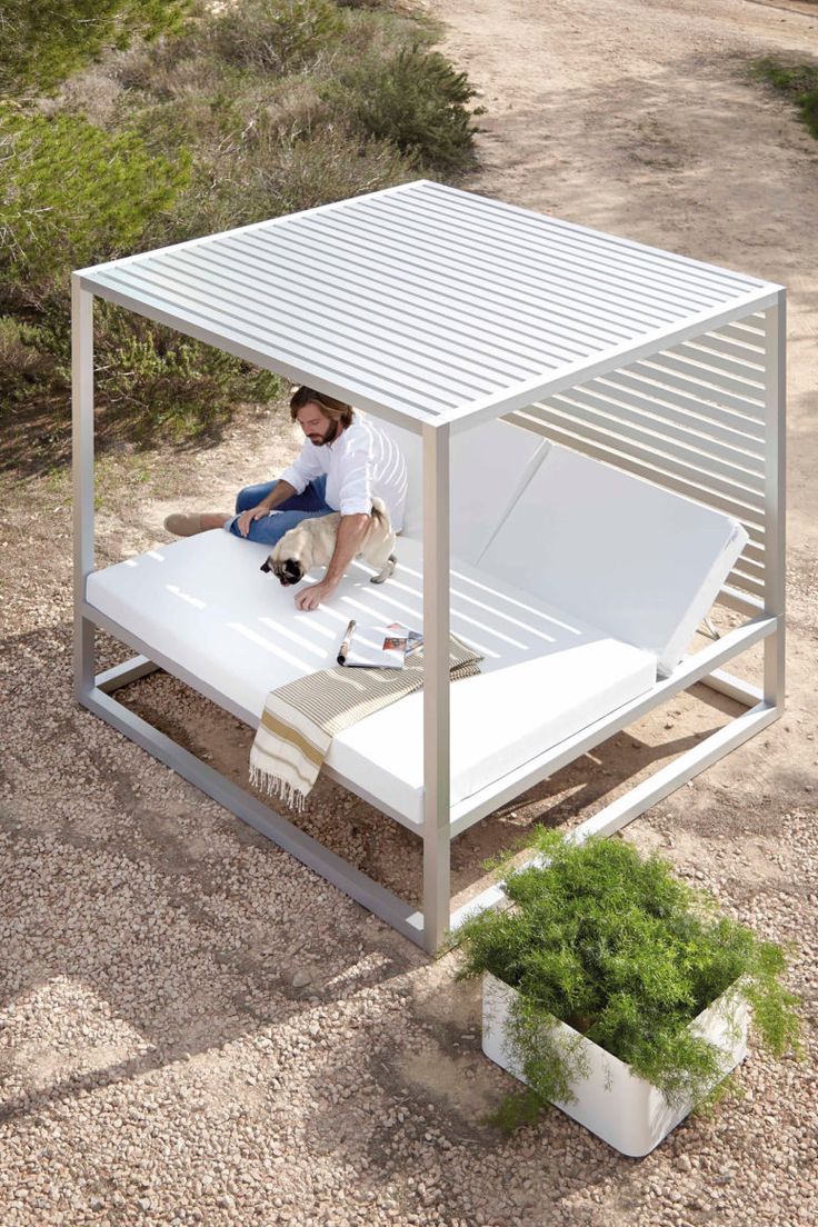 a man sitting on top of a white bed in the middle of a dirt field