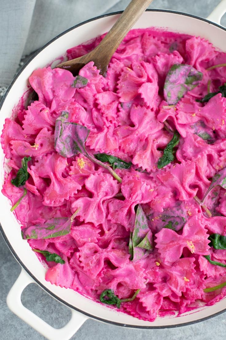 a pot filled with pink pasta and spinach on top of a gray table cloth