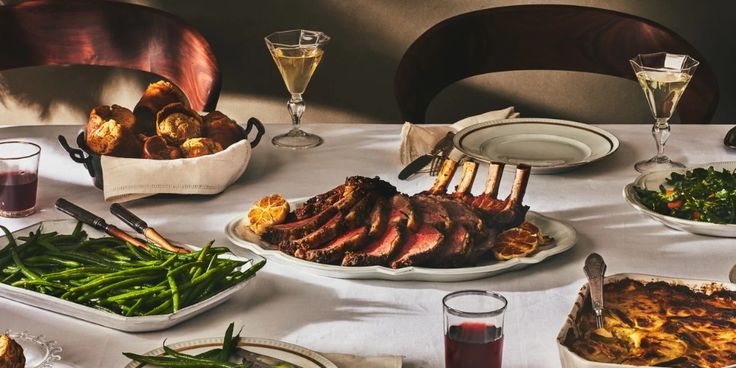 a dining table with plates and glasses filled with food, including meats and vegetables