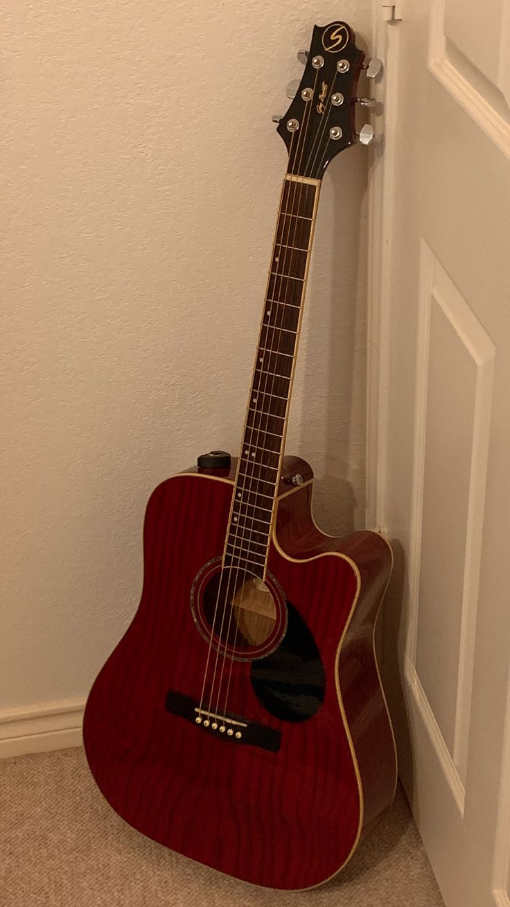 an acoustic guitar leaning against the wall in front of a door with its head propped up