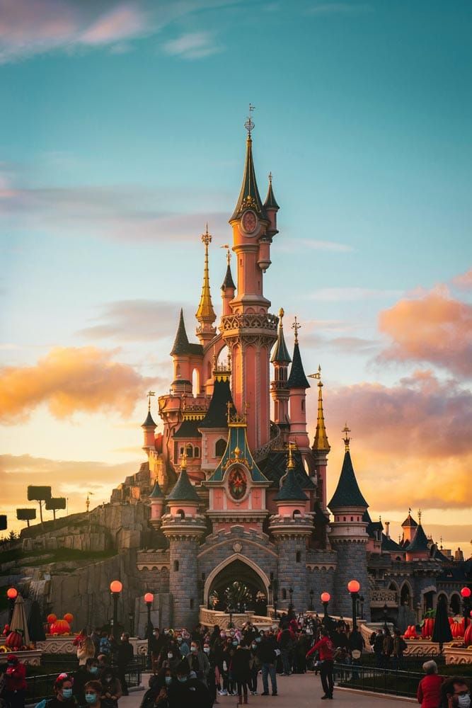 people are standing in front of a castle with turrets and spires at sunset or dawn