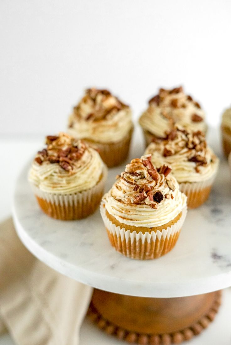 several cupcakes are sitting on a white cake platter with walnut toppings