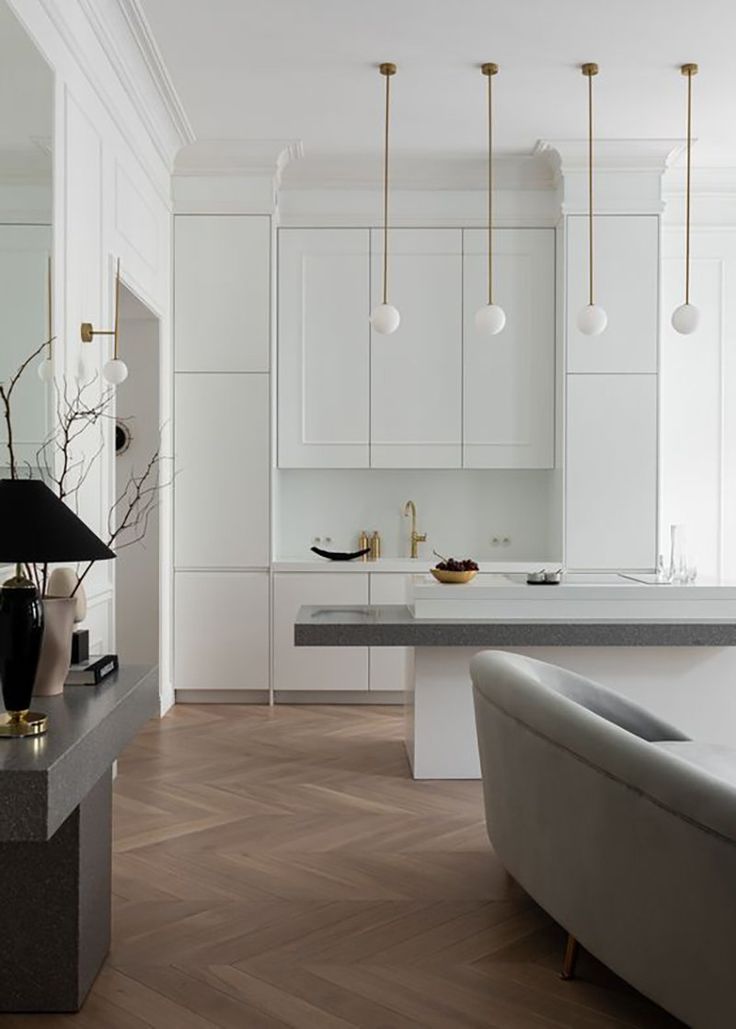 a modern kitchen with white cabinets and marble counter tops, gold accents on the pendant lights