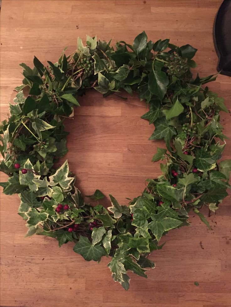 a wreath made out of green leaves and red berries on a wooden table with a black boot