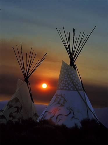 two teepees with the sun setting behind them