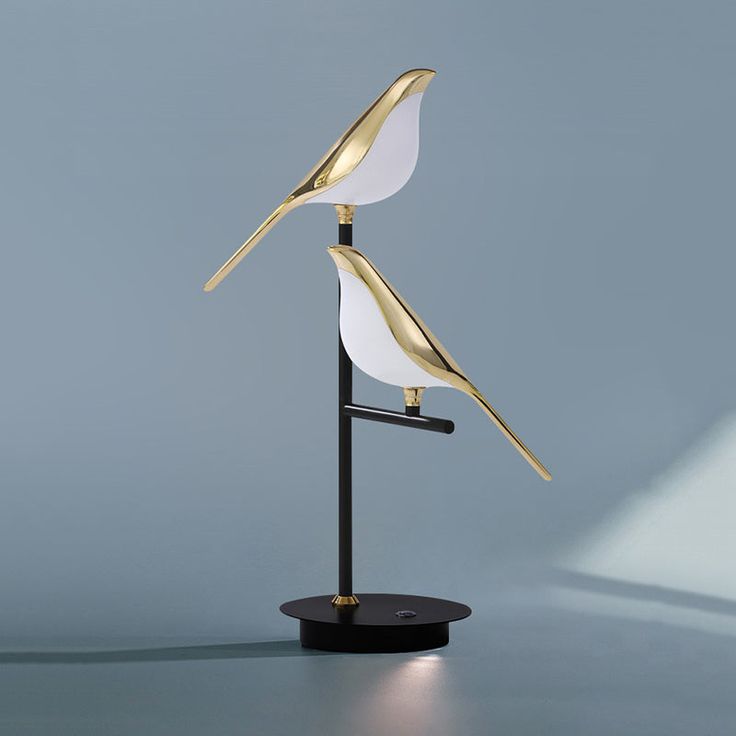 a lamp that is sitting on top of a black stand with a white and gold bird on it