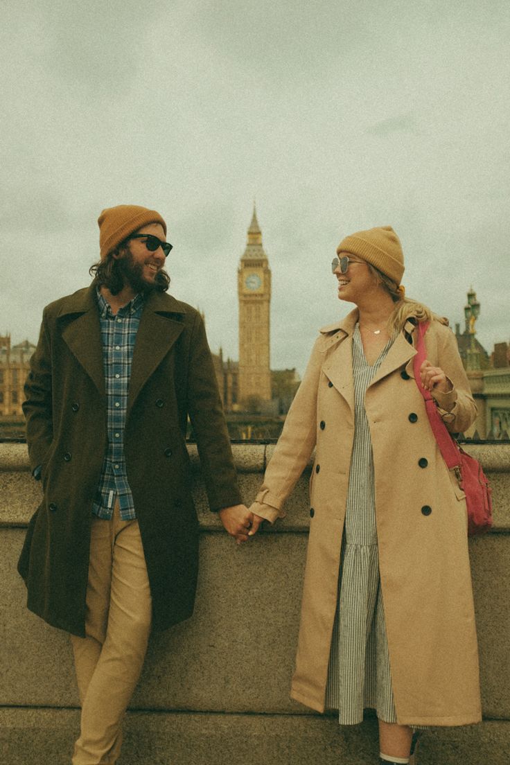 two people standing next to each other holding hands and looking at the sky with a clock tower in the background