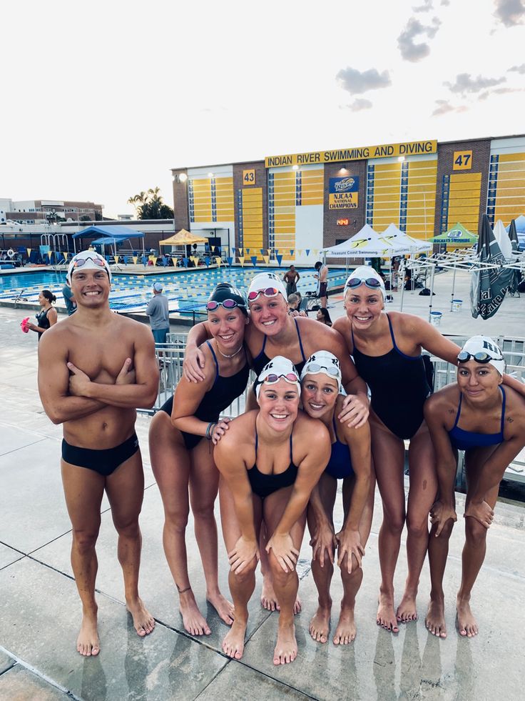 a group of women standing next to each other in bathing suits on a swimming pool