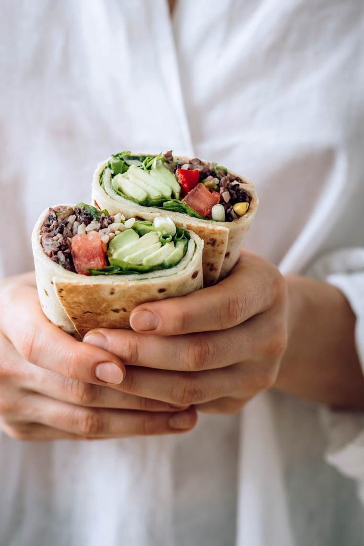 a person holding a wrap filled with veggies and other things in their hands