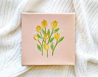 a pink square with yellow flowers on it sitting on a white bed sheet next to a pillow