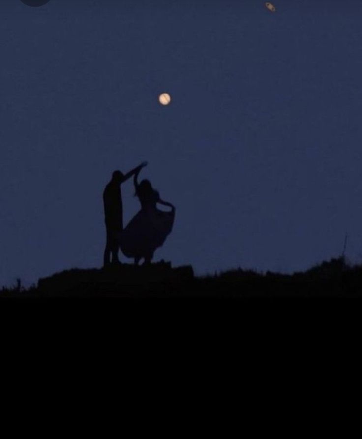 two people standing on top of a hill under a full moon at night with one holding the other's hand