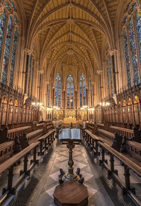 the interior of a cathedral with pews and stained glass windows on both sides,