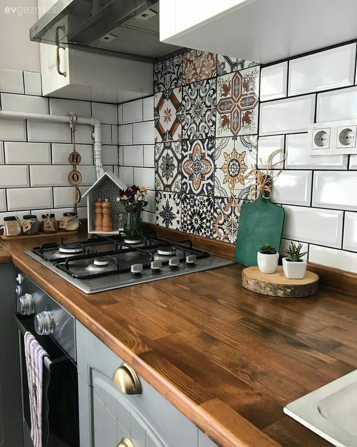 a kitchen with white tiles and wooden counter tops, an oven hood and stove top