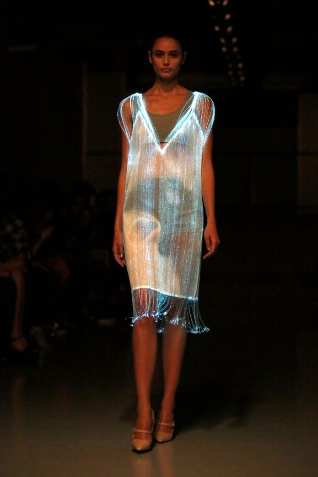 a woman is walking down the runway in a white dress with blue lights on it