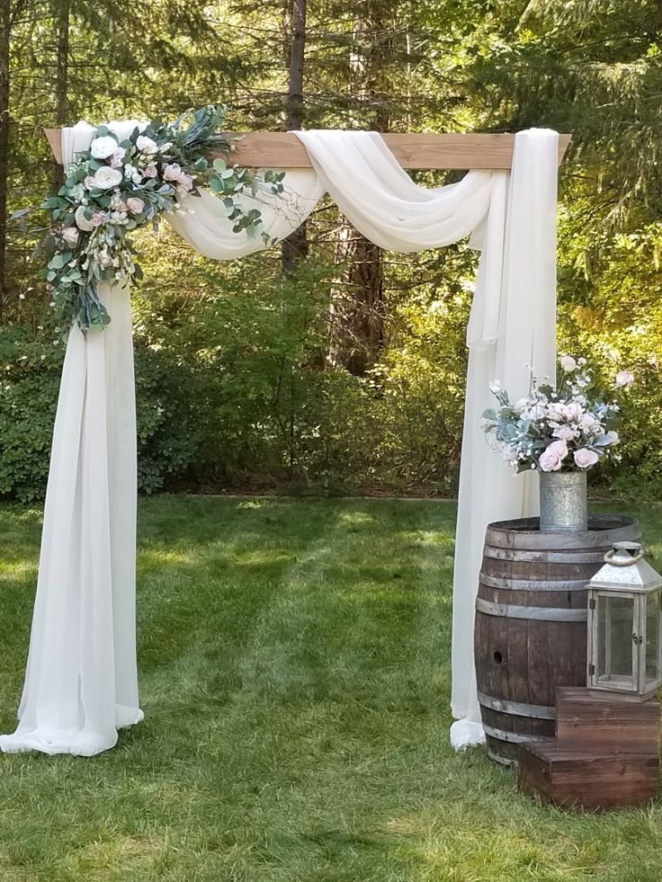 an outdoor wedding setup with white drapes, flowers and greenery on the grass