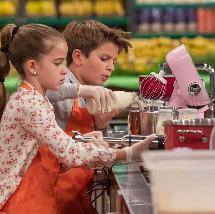 two children are preparing food in the kitchen together and one girl is using a mixer