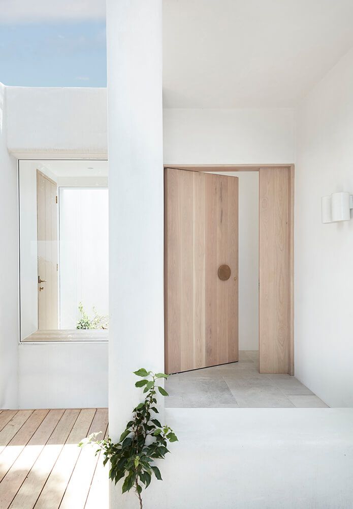 an open door in a white room with wooden flooring and plants on the side