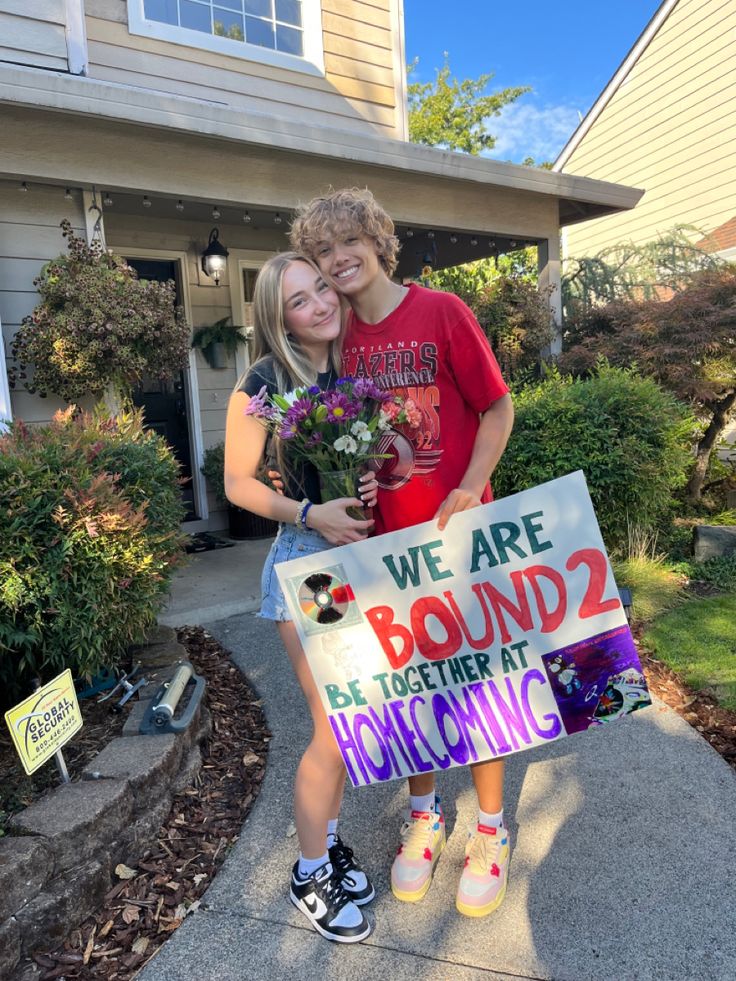 two girls holding flowers and a sign in front of a house that says we are bound 2 together