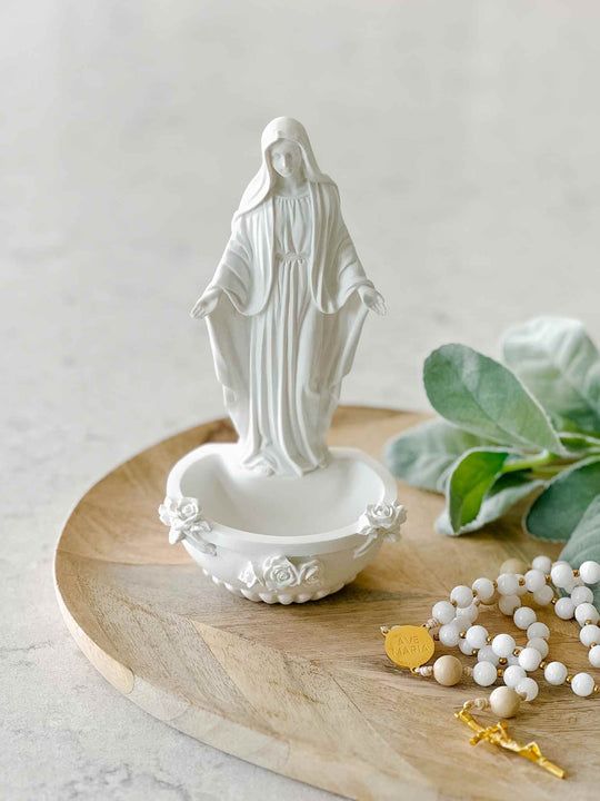 a white statue sitting on top of a wooden tray next to some beads and leaves