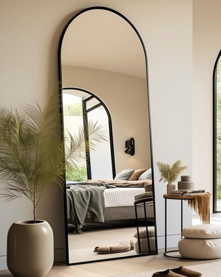 a large mirror sitting on top of a wooden floor next to a plant in a vase