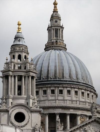 the dome of an old building with statues on it's sides and a clock tower in the background