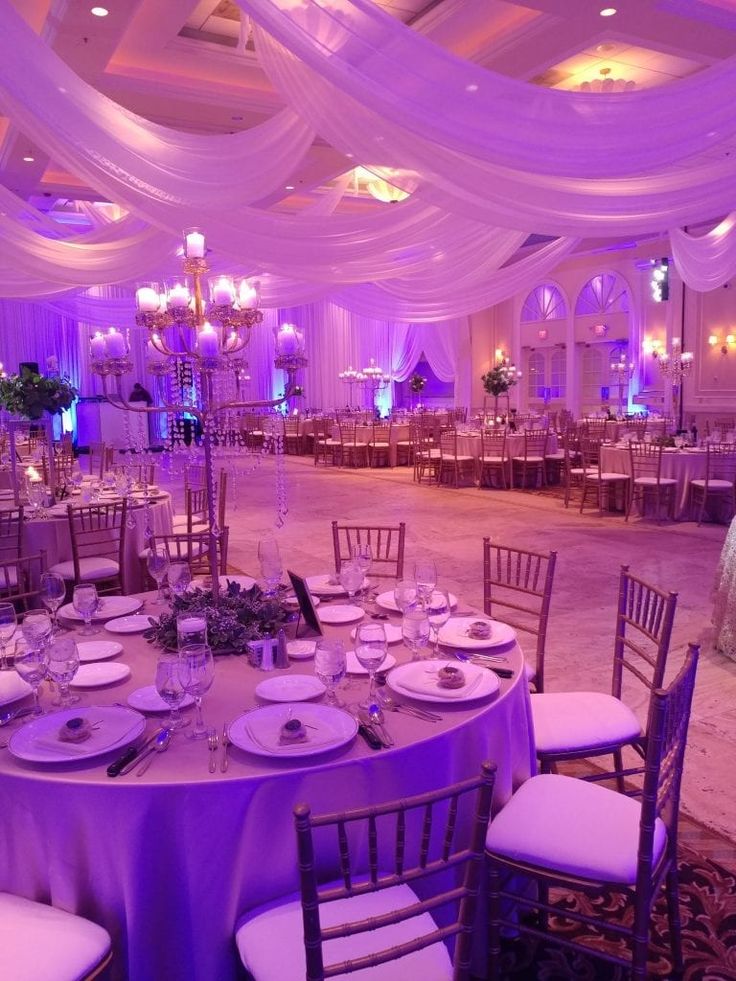 a banquet hall with tables and chairs set up for an event or function, purple lighting is on the ceiling