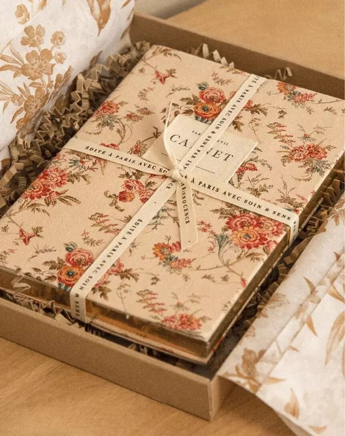 an open gift box on a table with floral fabric and ribbon wrapped around the lid