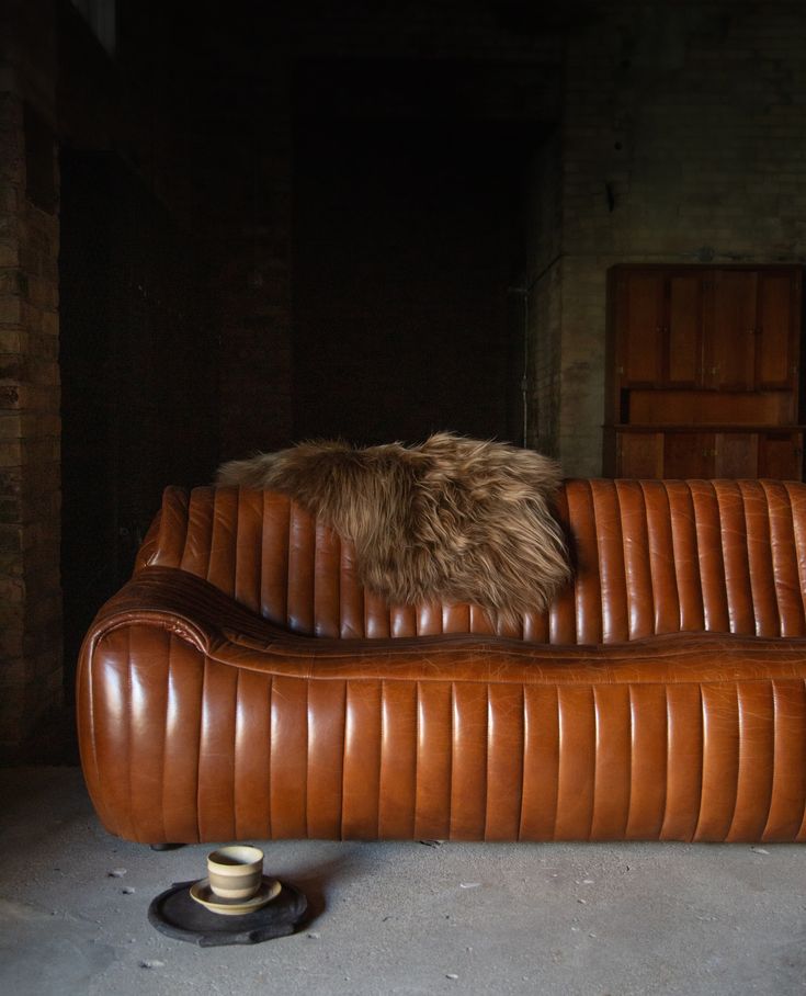 a brown leather couch with a furry pillow on it's back and the seat up