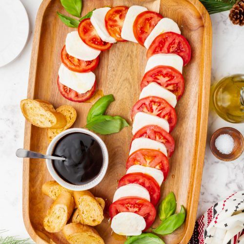 a wooden platter filled with sliced tomatoes and mozzarella chips, next to a cup of black sauce