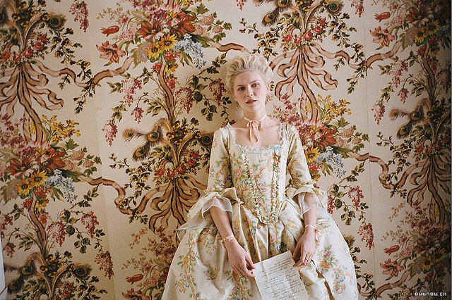 a woman sitting on top of a bed in front of a floral wallpaper