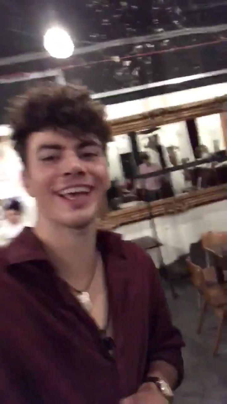 a young man is smiling while standing in a room with chairs and tables behind him