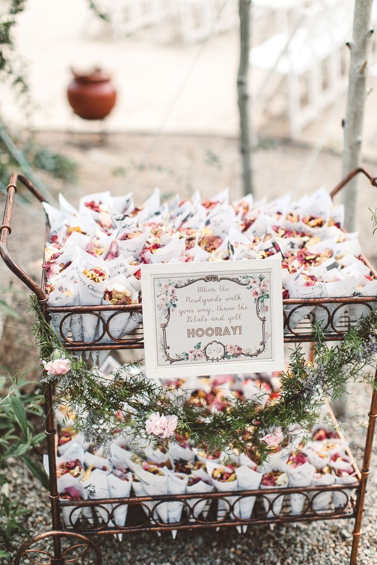 a metal cart filled with lots of paper and flowers on top of a gravel ground