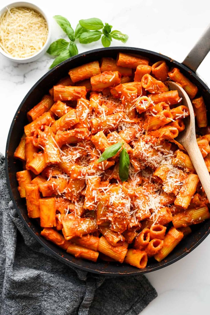 a skillet filled with pasta, sauce and parmesan cheese on a white table