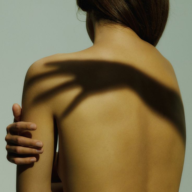 a woman's back with the shadow of a tree branch on her shoulder and arm