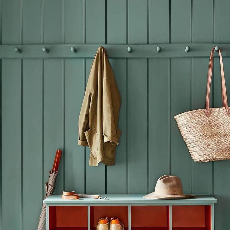 a coat rack with two coats hanging on the wall next to a hat and umbrella