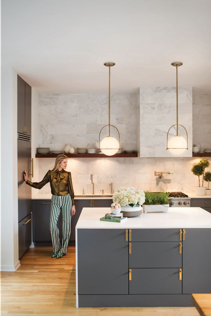 a woman standing in a kitchen next to a counter with flowers on top of it