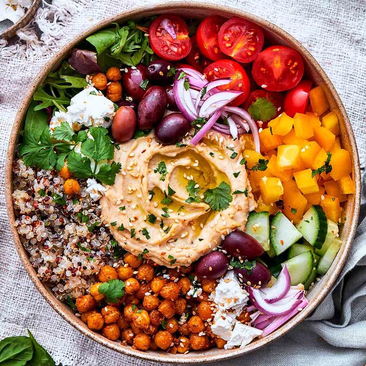 a bowl filled with different types of vegetables and hummush sauce on top of it