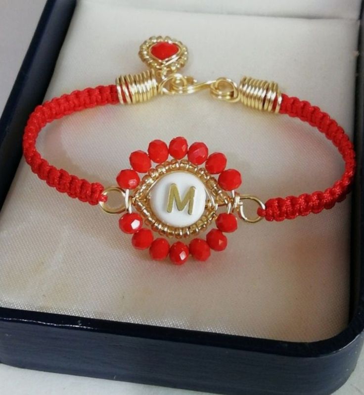 a red beaded bracelet with the letter m on it is sitting in a box