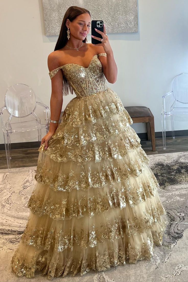 Make an unforgettable entrance in this eye-catching off-the-shoulder gold-sequin ruffle multi-layer long gown. Featuring exquisite gold-sequin lace, a deftly crafted lace-up back, and multiple layers of tulle for a luxurious effect, this showstopping dress is the perfect choice for any special occasion. Be the belle of the ball!#prom#promdresses#promgown#formaldress#formaloutfit#seniorpromdress#promgown#blacktieeventdresses Chiffon Wedding Dress Beach, Sequin Ball Gown, Tiered Tulle Skirt, Champagne Prom Dress, Elegant Ball Gowns, Prom 2024, Evening Party Gowns, Lace Prom Dress, Prom Inspo