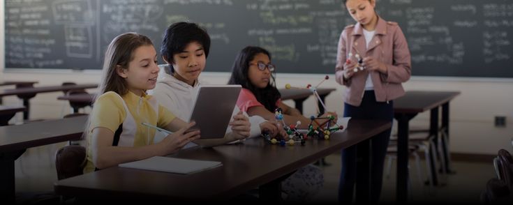 children are sitting at desks in front of a blackboard