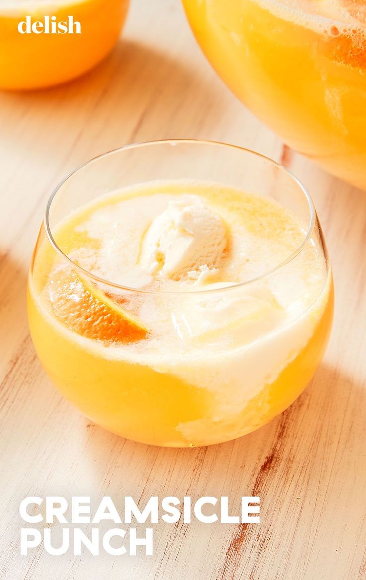 two glasses filled with orange juice and ice cream on top of a wooden table next to an orange slice