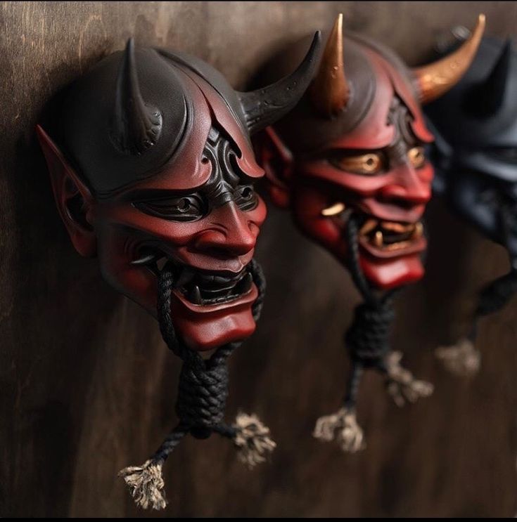 two red and black masks with horns hanging on a wall next to another one wearing a helmet