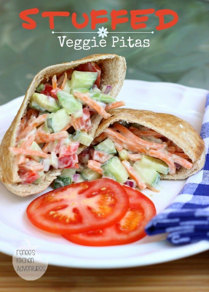 a sandwich cut in half on a white plate with tomatoes and cucumbers next to it