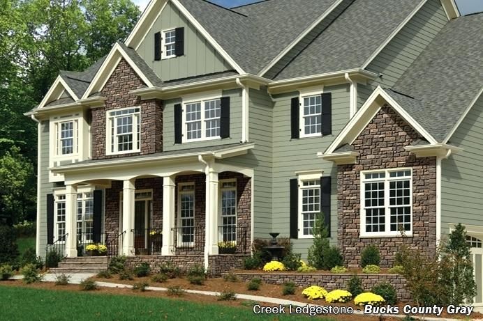 a large house with lots of windows and stonework on the front porch, surrounded by lush green grass