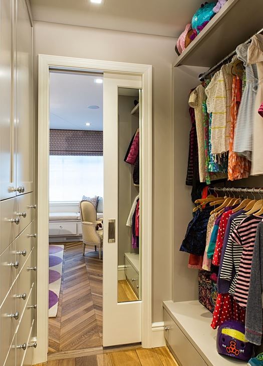 an open closet with clothes hanging on the wall, and a door leading to another room